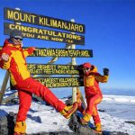 Climbers celebrating at Uhuru Peak summit on Mount Kilimanjaro during sunrise in Tanzania