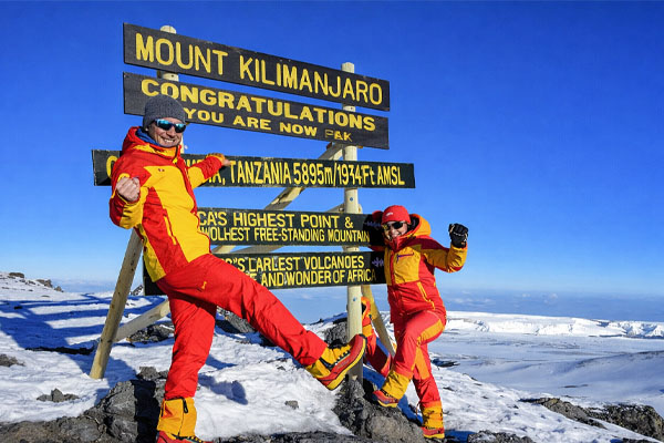 Climbers celebrating at Uhuru Peak summit on Mount Kilimanjaro during sunrise in Tanzania